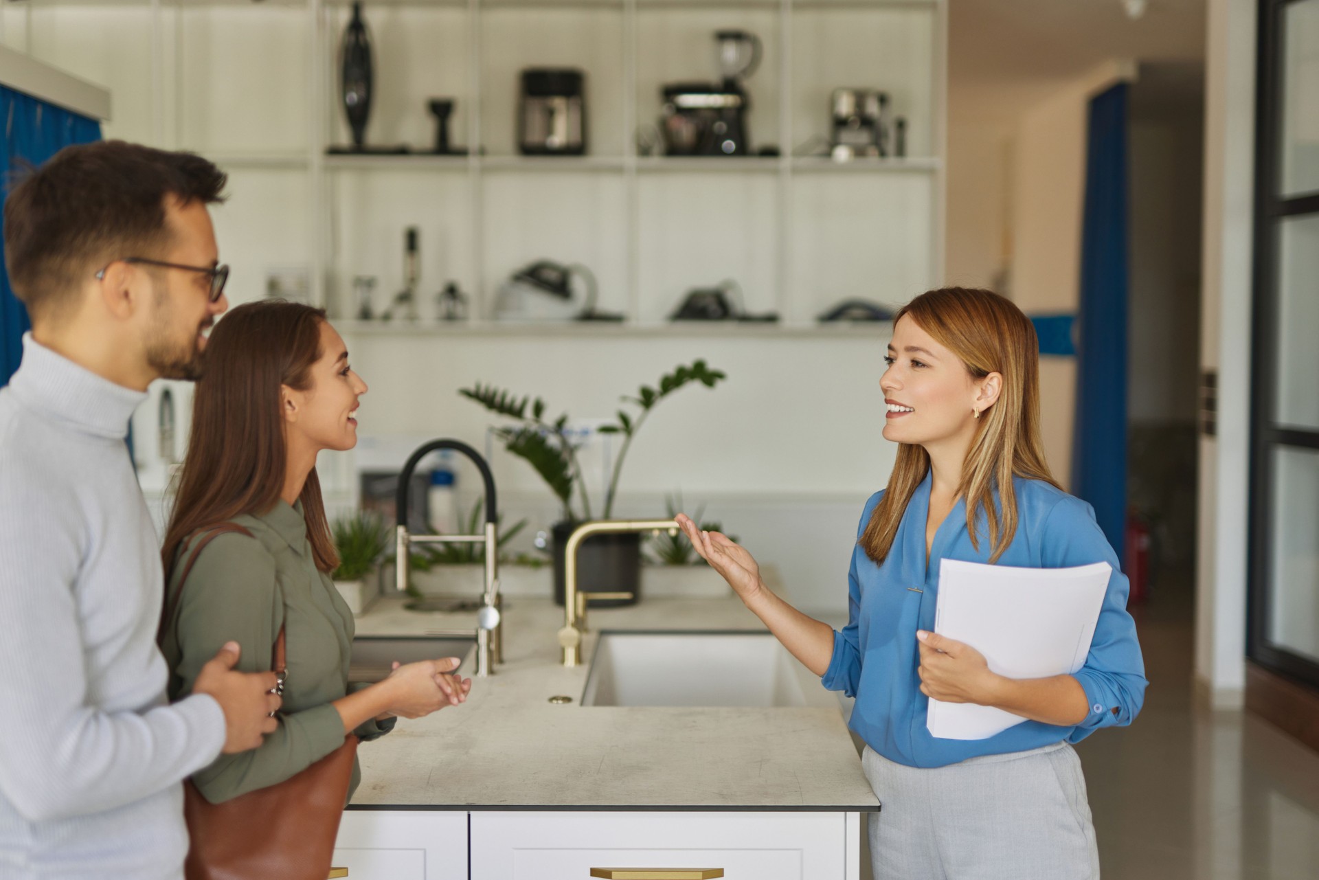 Female shop assistant helping young couple choose new kitchen faucet